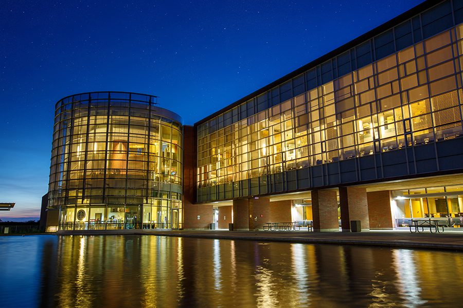 Ontario Tech’s North Oshawa Campus Library glowing gold against a deep blue evening sky, reflected in the pond